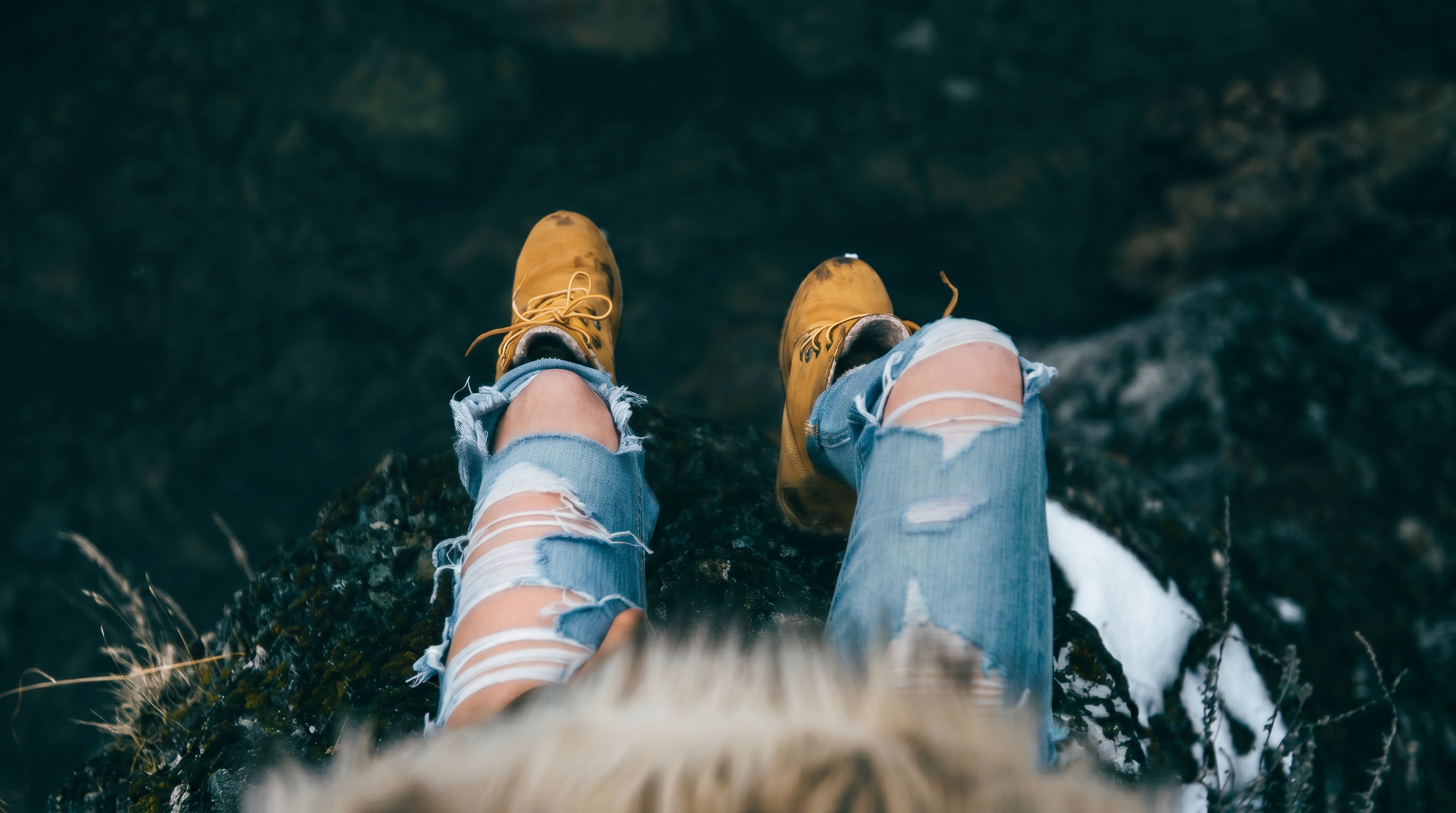 Timberland Canada campaign hero — POV looking down from a cliff edge, yellow nubuck boots and ripped jeans on dark moss-covered rock, Blue Mountains